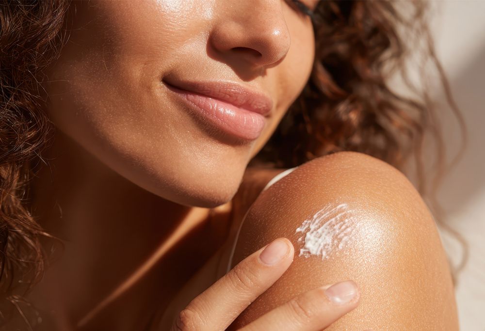 A smiling person applies sunscreen lotion to their shoulders.   