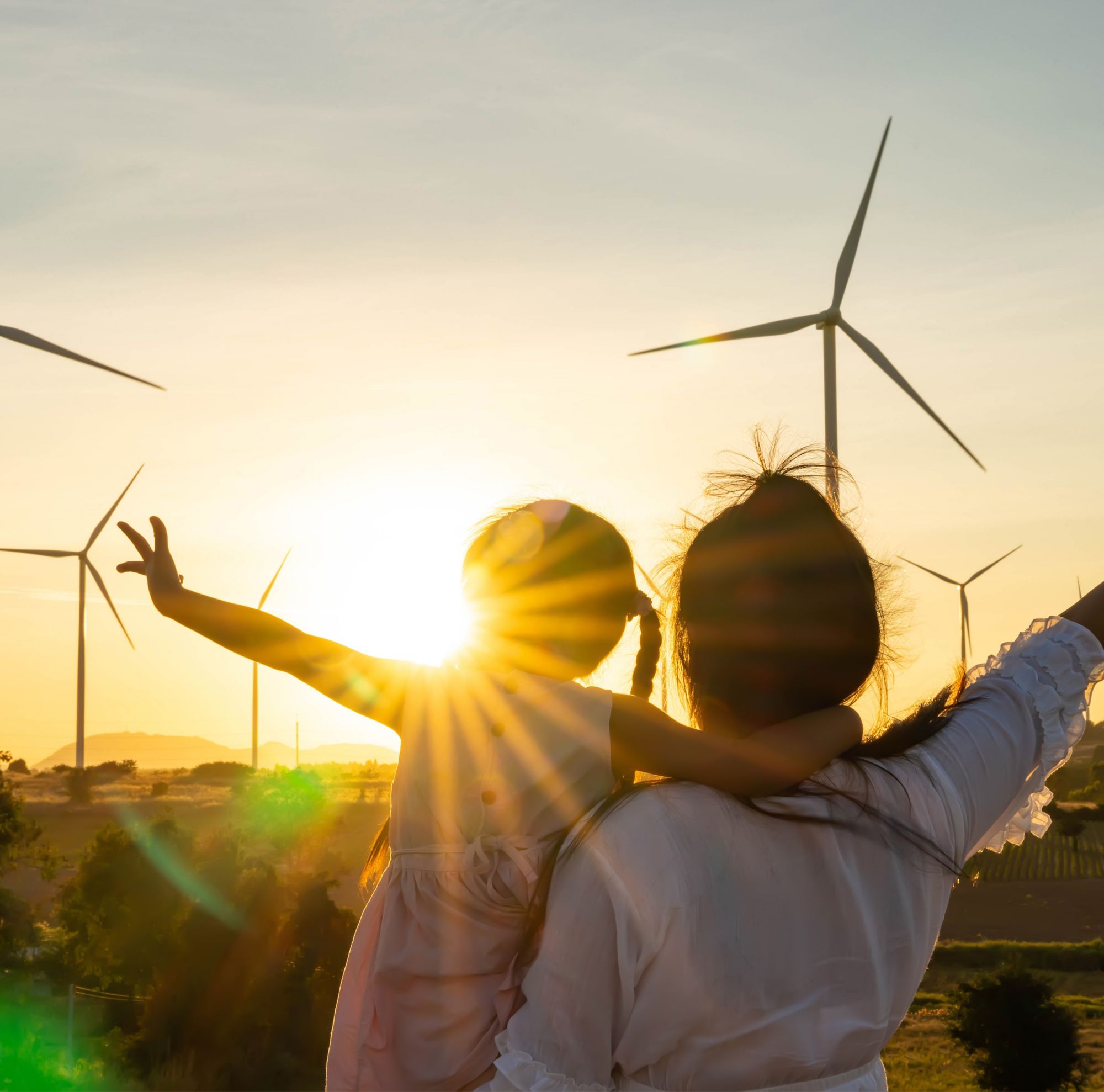 Une femme portant un enfant lors d’un coucher de soleil devant des éoliennes 