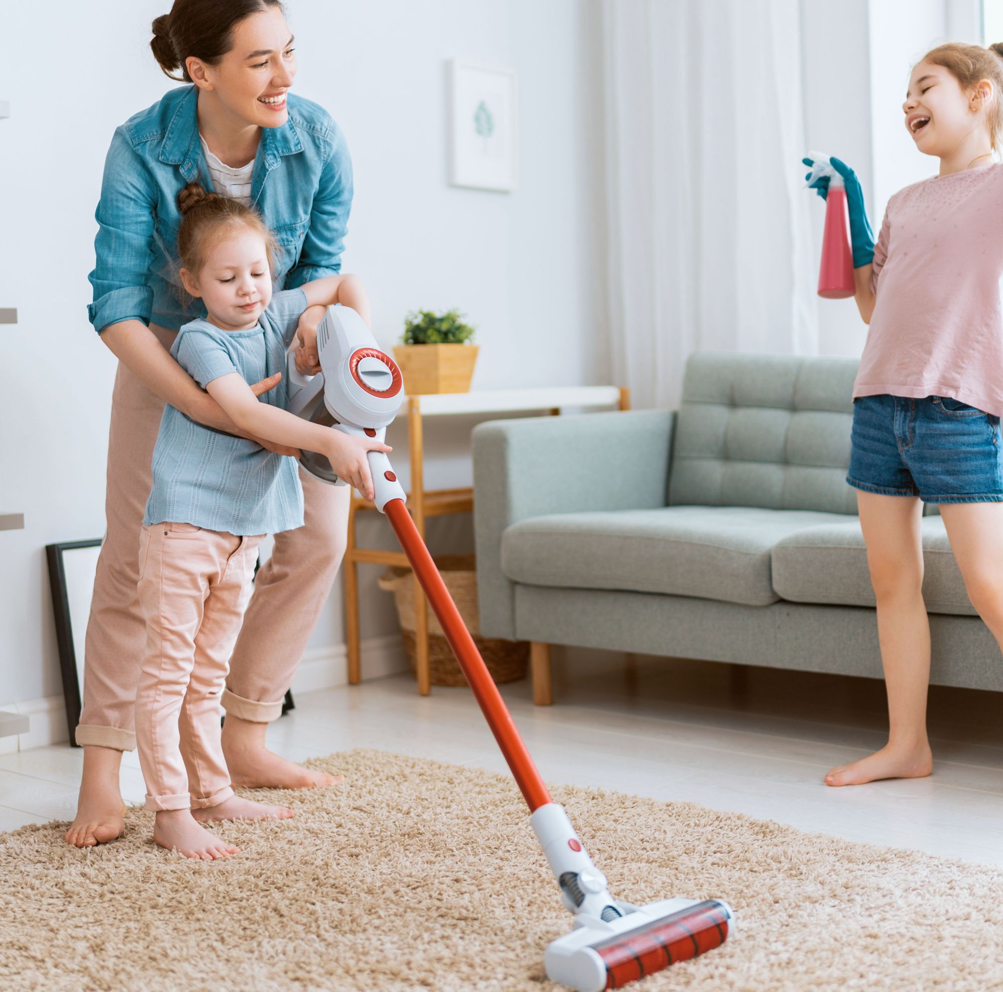 A woman vacuuming a rug with a child as another child laughs. 