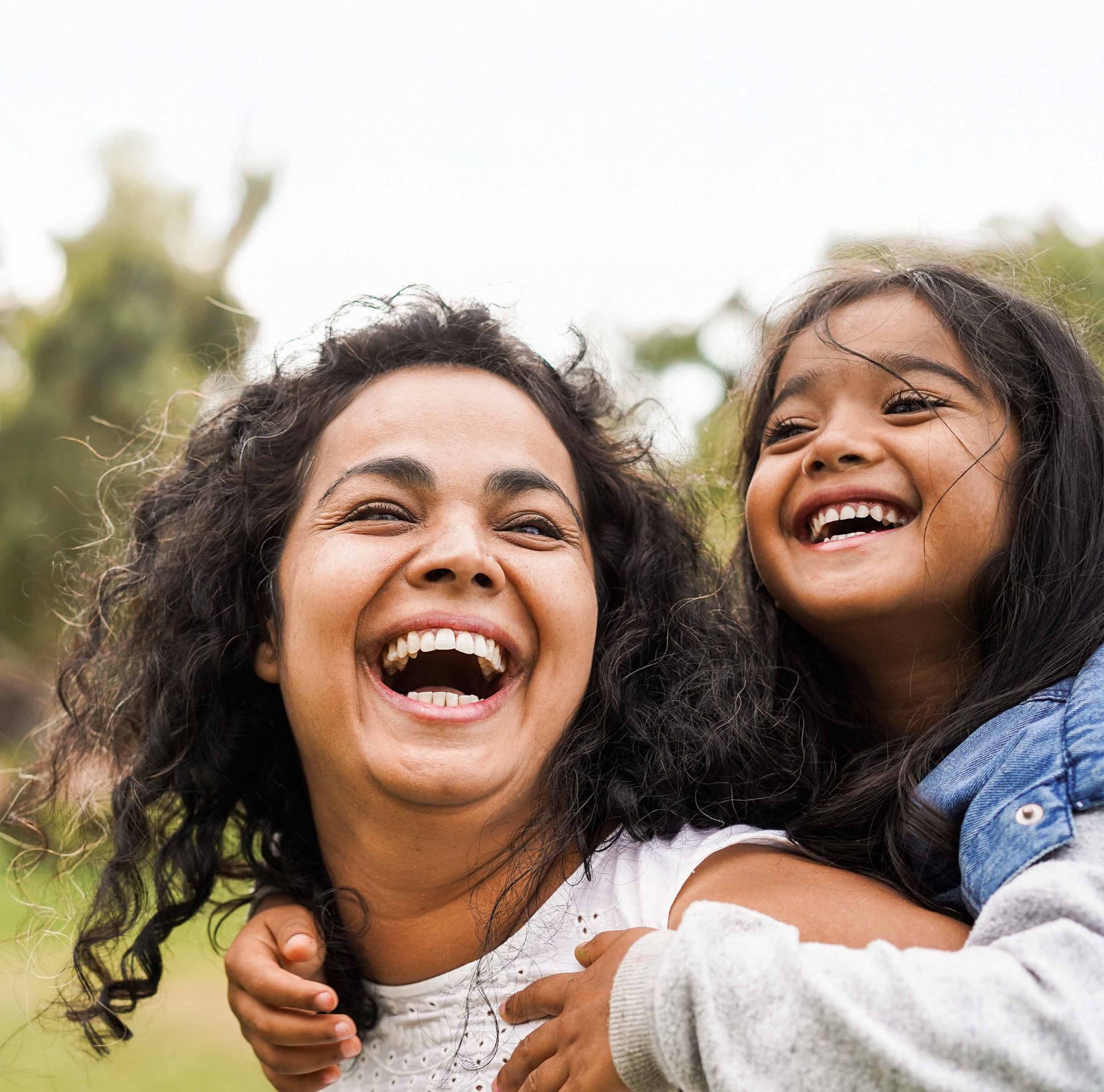 A woman and young girl smiling outside. 
