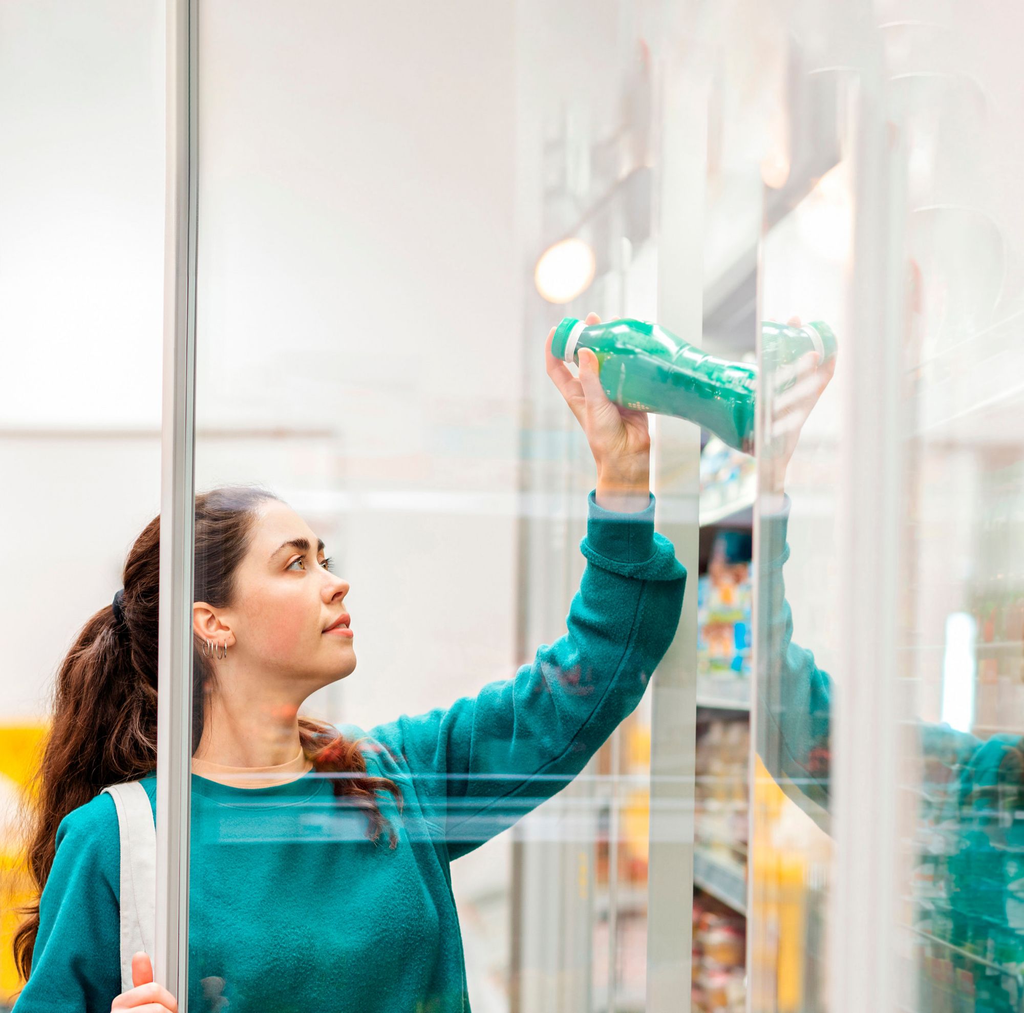 A person grabs a green beverage bottle from a refrigerated shelf. 