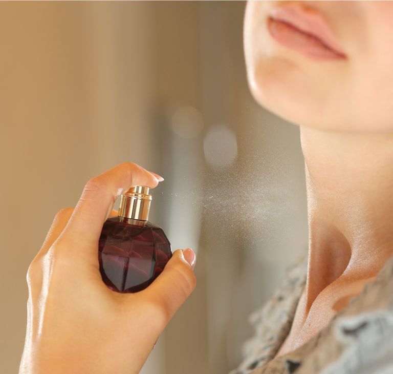 A person sprays a bottle of perfume on their neck.  