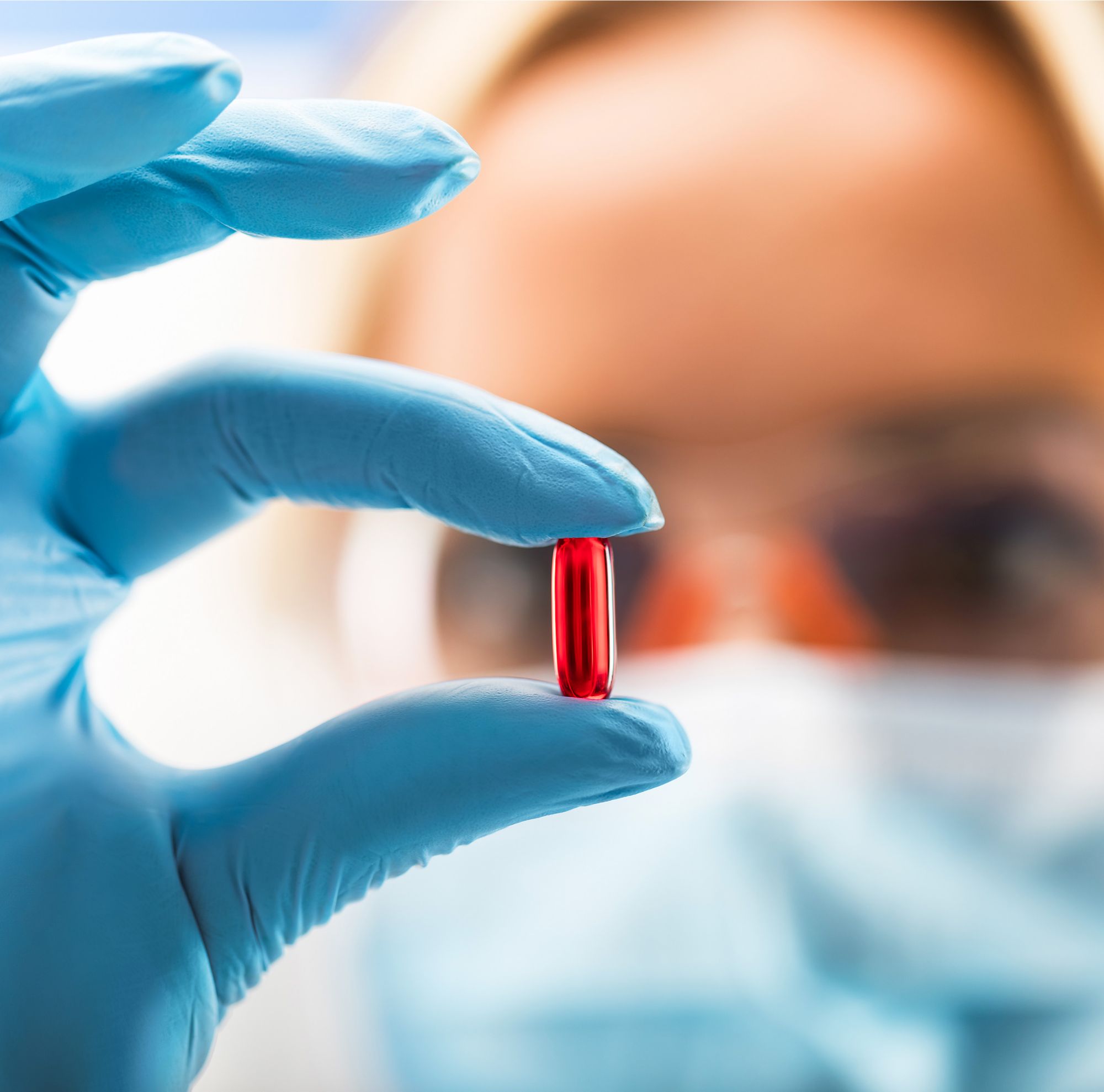 A masked scientist inspecting a red pill 