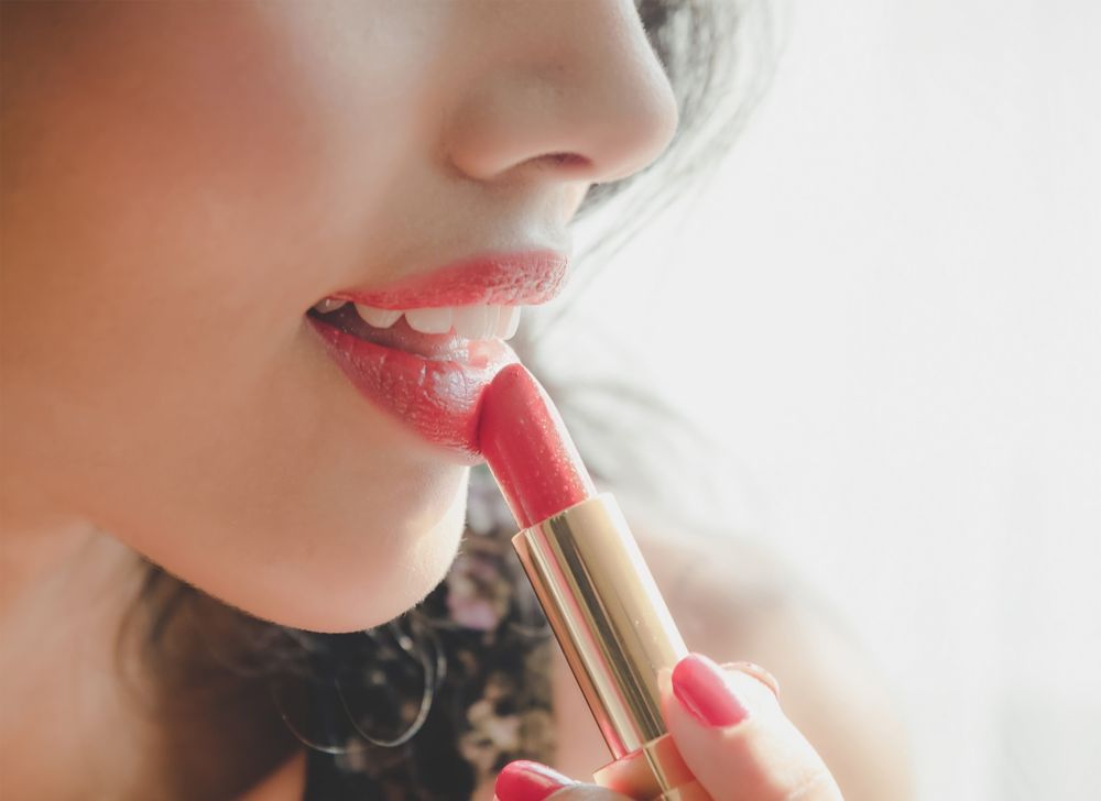 Coral lipstick is applied to lips.   