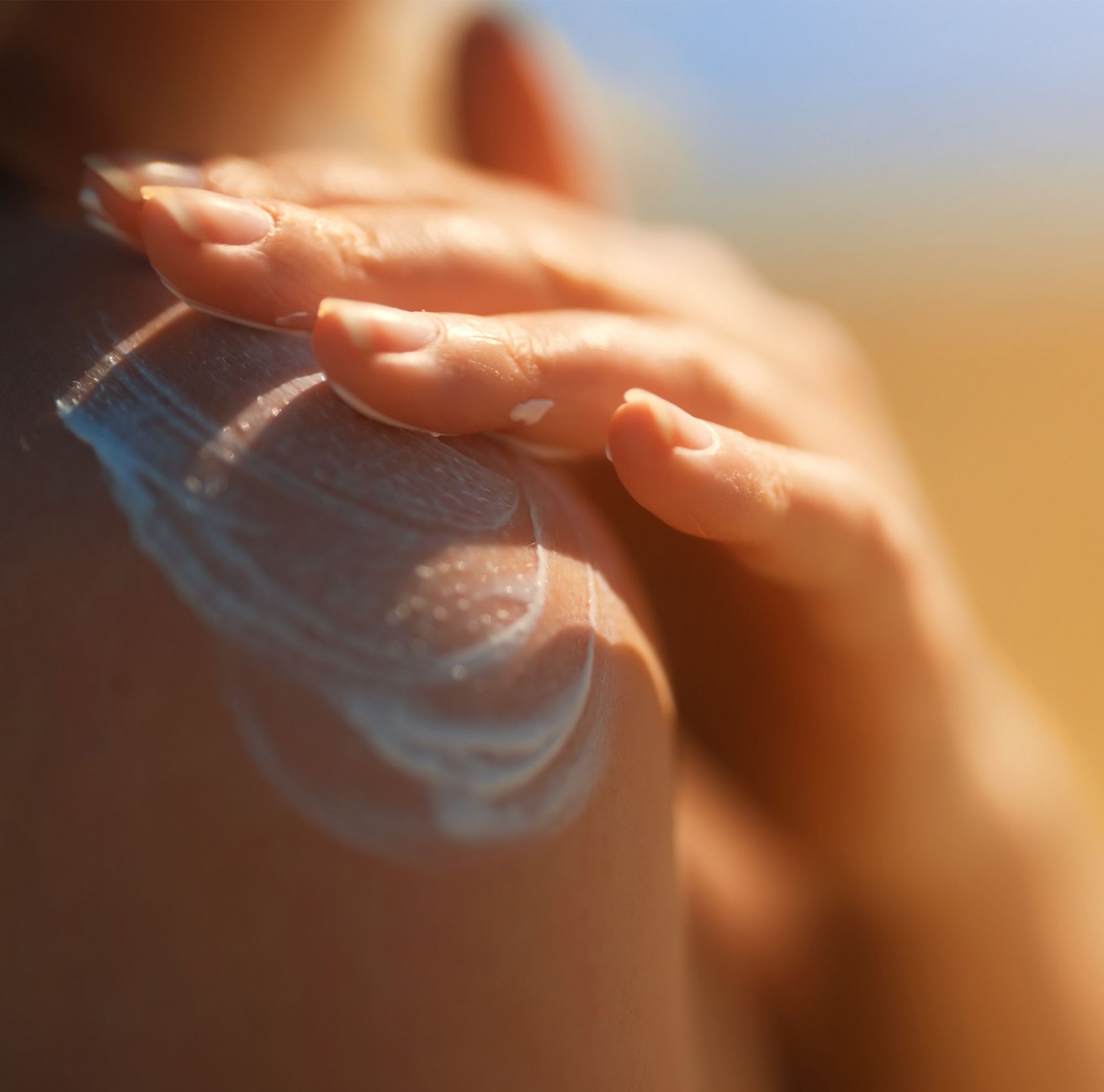Close-up of a person applying sunscreen lotion to their shoulder. 