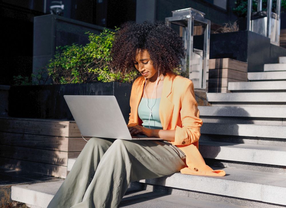 A woman uses her laptop while sitting on a staircase. 