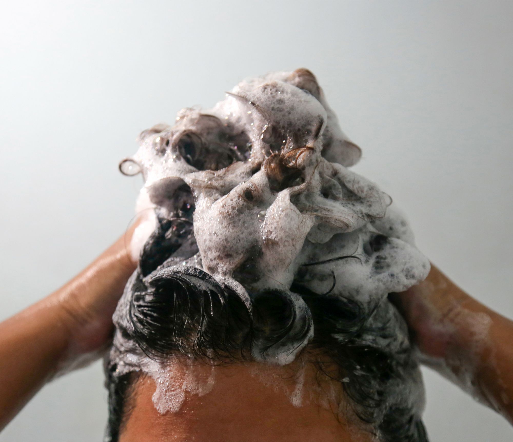 Woman washes and lathers her hair with sulfate-free shampoo. 
