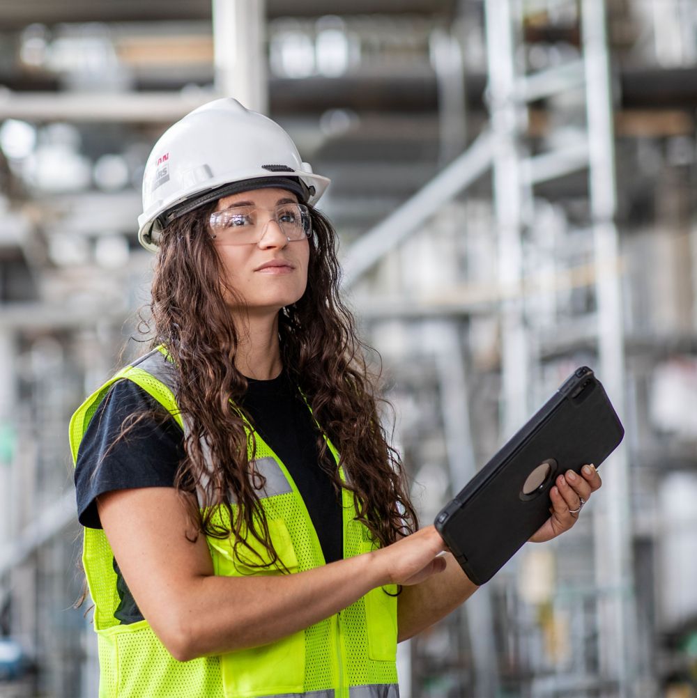 Woman wearing a white hard hat working in a factory. 