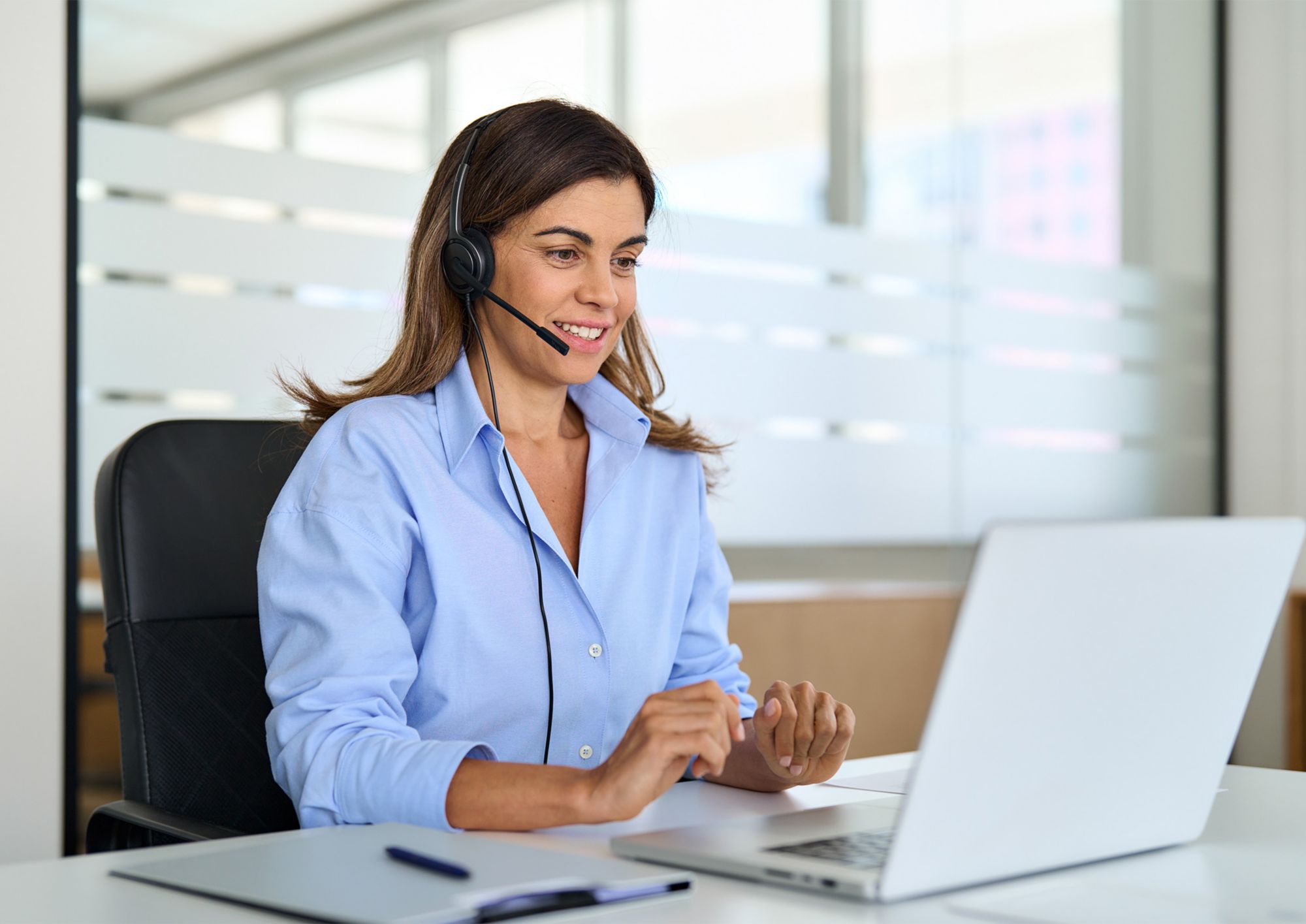 A person wearing a headset microphone works on a laptop computer.   