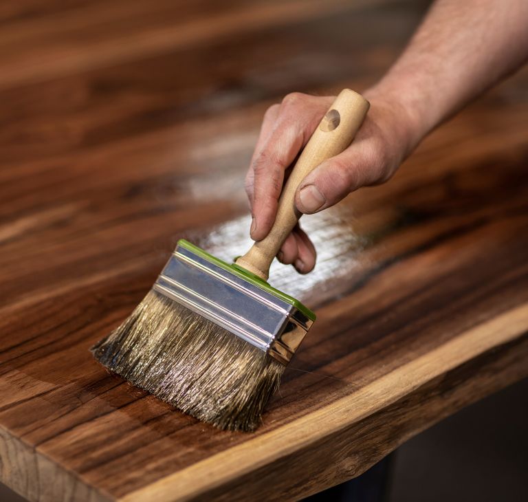 A large brush is used to brush stain on wood. 