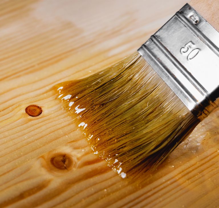 A paint brush applies stain to wood. 