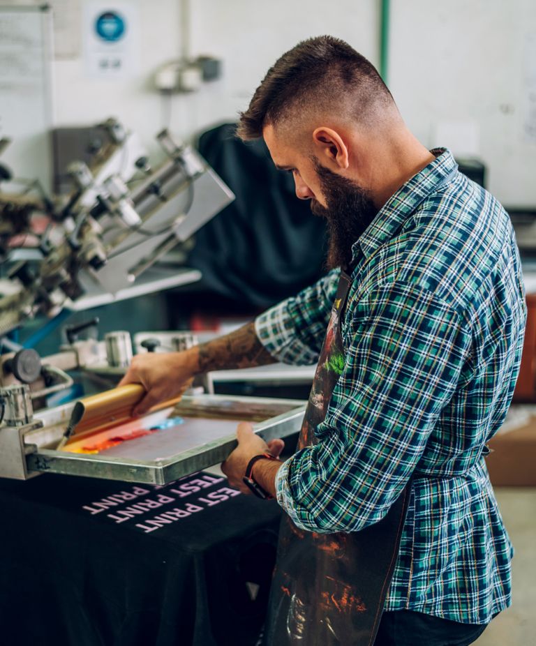 A man presses ink onto a shirt in a printshop. 