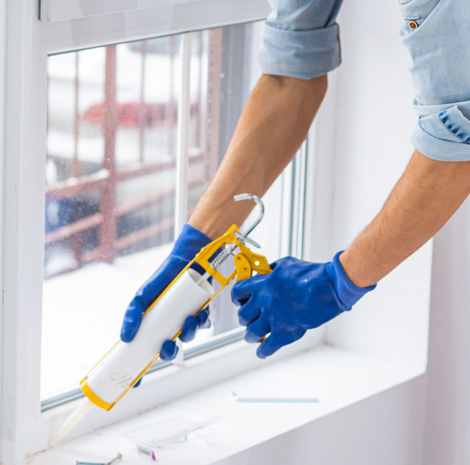 A person applies caulk around a window. 