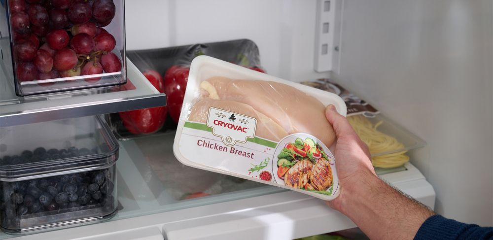 A person holds wrapped chicken breast that is inside a refrigerator 
