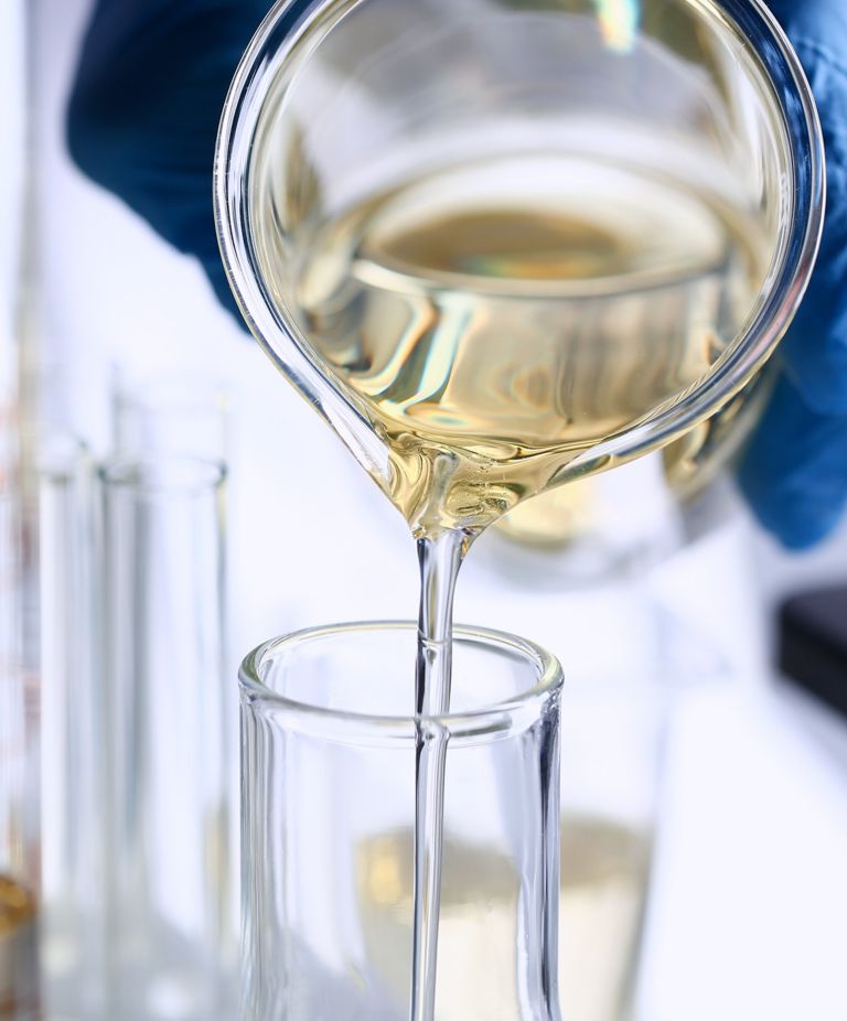 Yellow liquid is poured from a glass jar into a glass beaker. 
