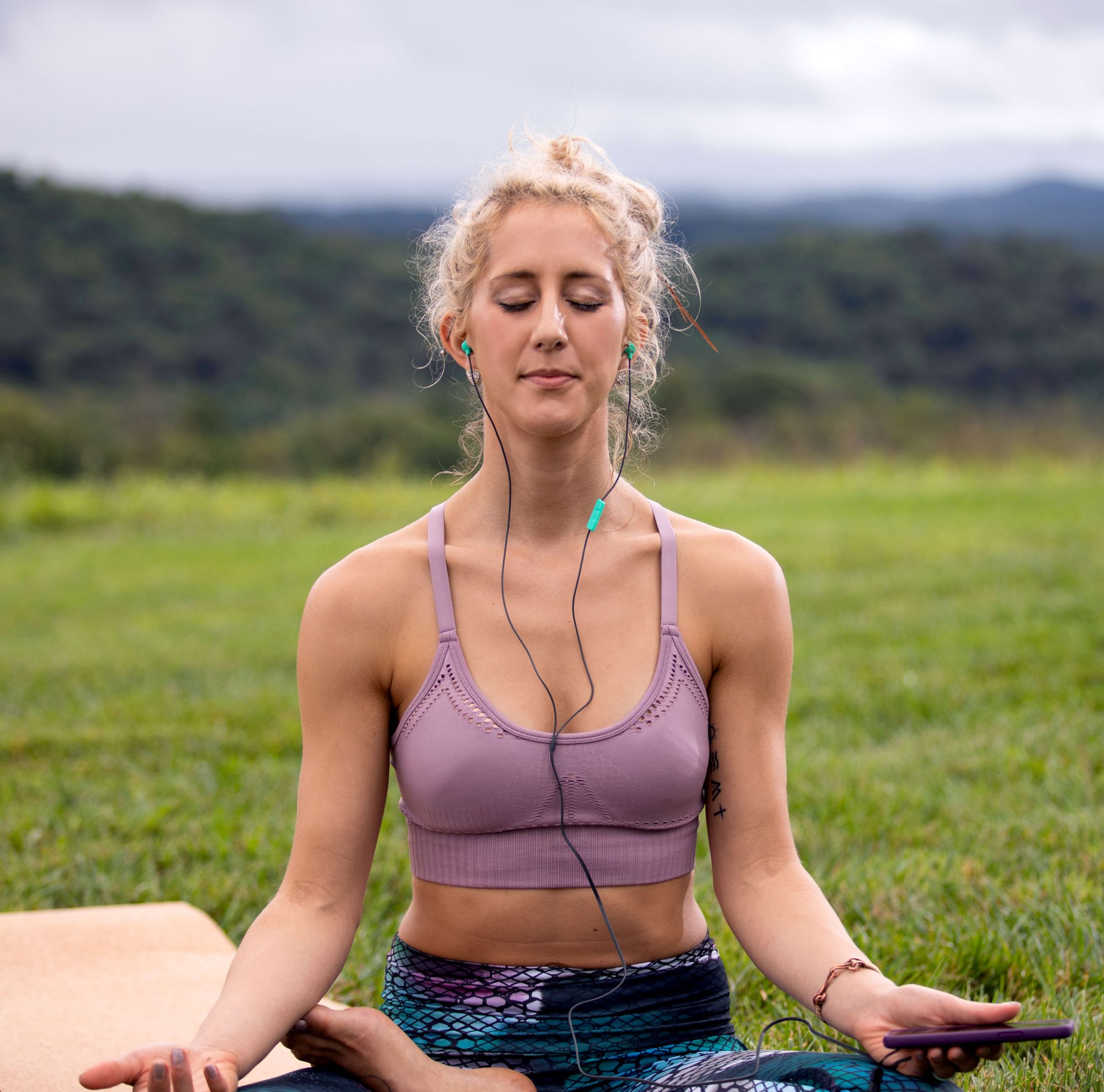 Person meditating outdoors with earbuds in. 