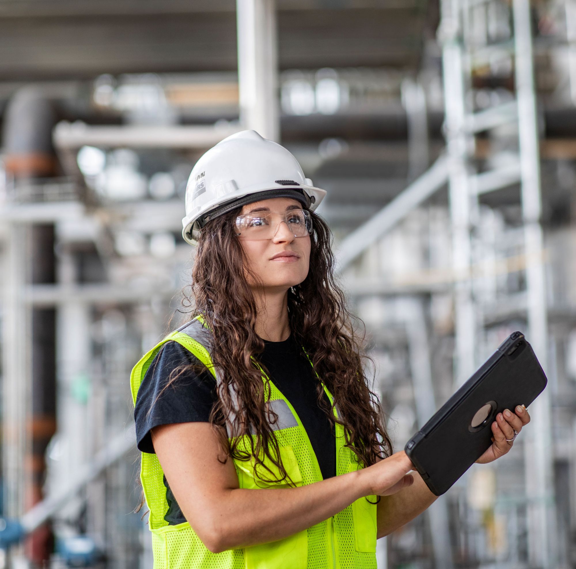 Una joven ingeniera con gafas de seguridad, casco y chaleco de seguridad en el sitio.  