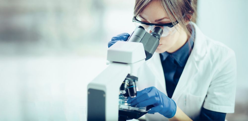 Young female scientist looking through microscope. 