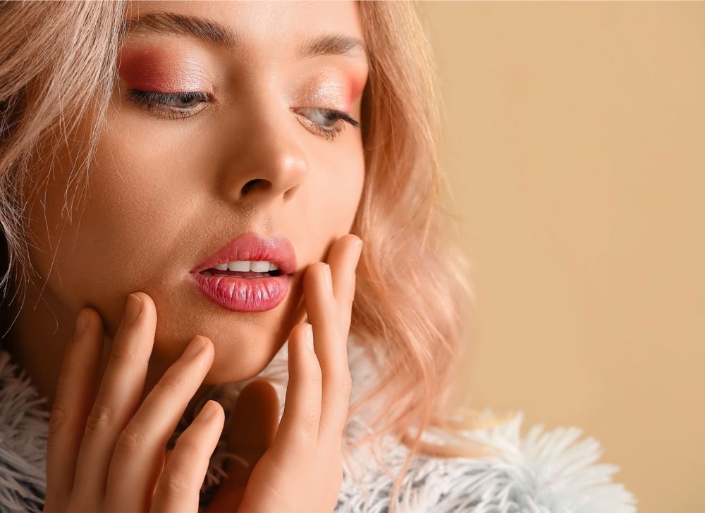 A person wearing pink eyeshadow and lipstick touches their cheeks.   