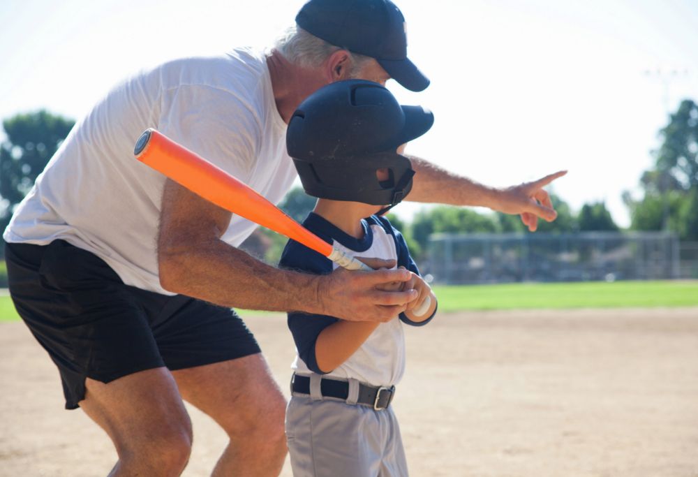 A man helping a little boy hold and swing a baseball bat. 