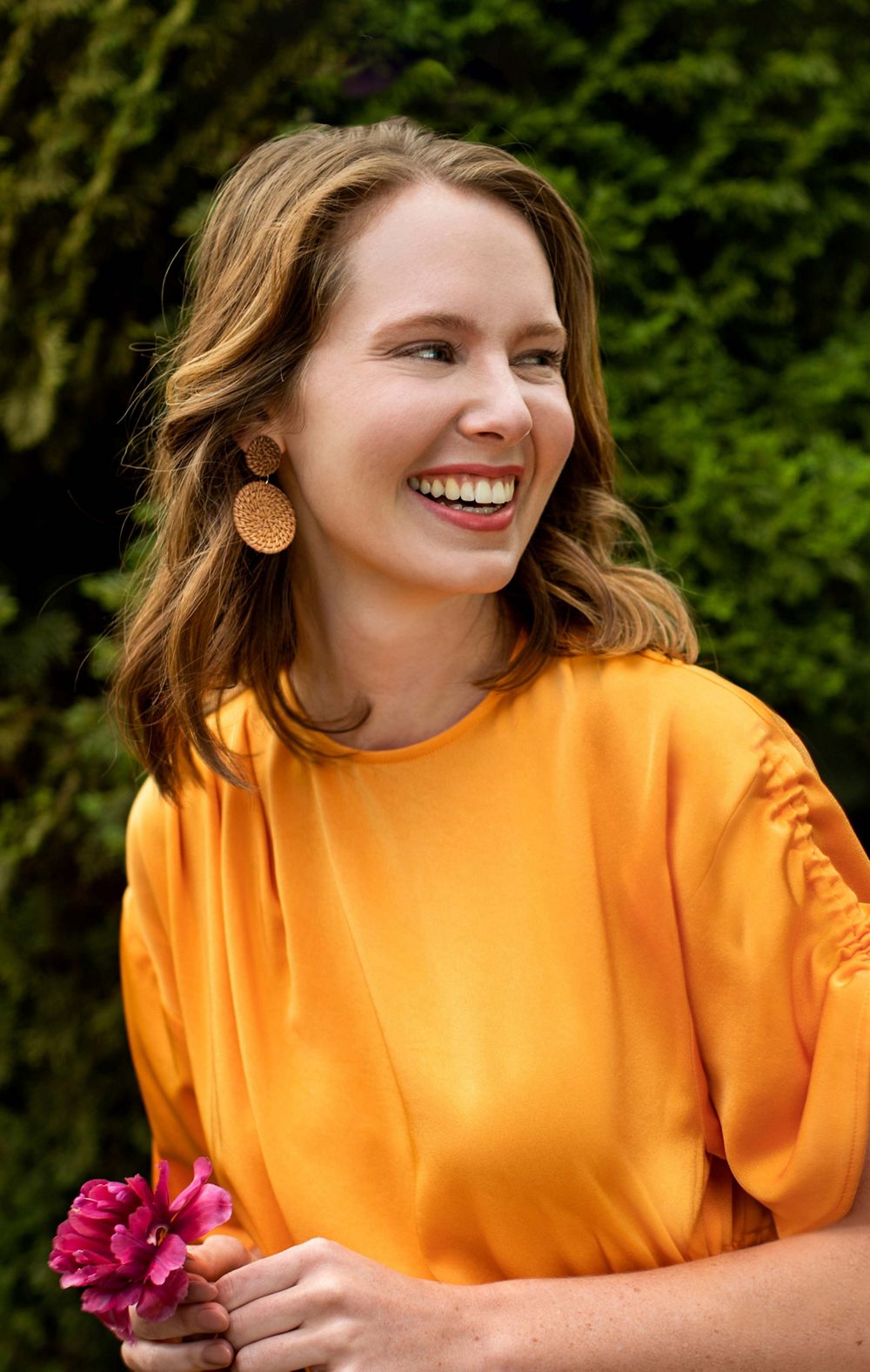 A woman in a yellow shirt smiles while holding a flower. 