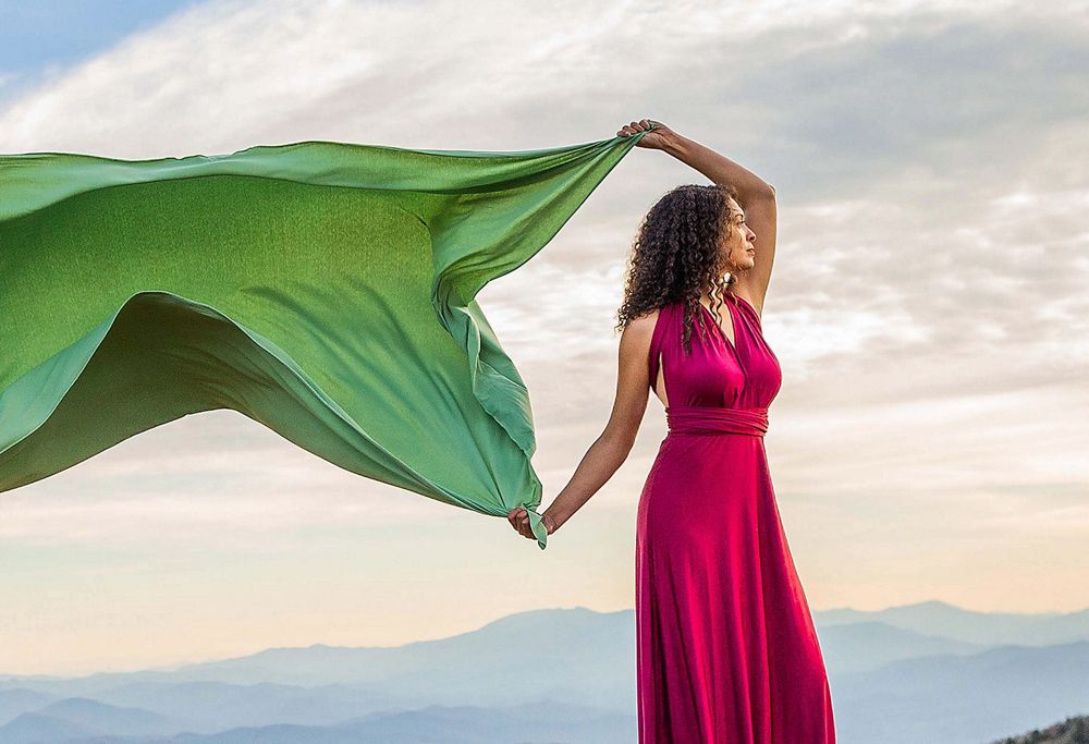 A person in a gown holds a large piece of fabric that waves in the wind. 